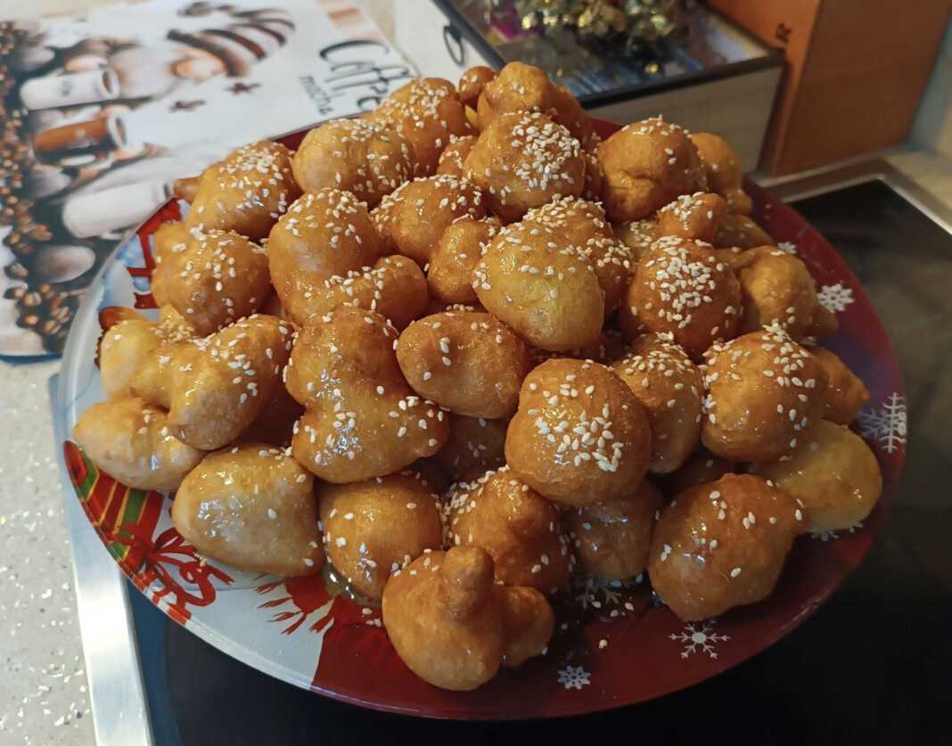 Μια πιατέλα γεμάτη χρυσαφένιους, στρογγυλούς λουκουμάδες, περιχυμένους με άφθονο μέλι και πασπαλισμένους με καβουρδισμένο σουσάμι και κανέλα.