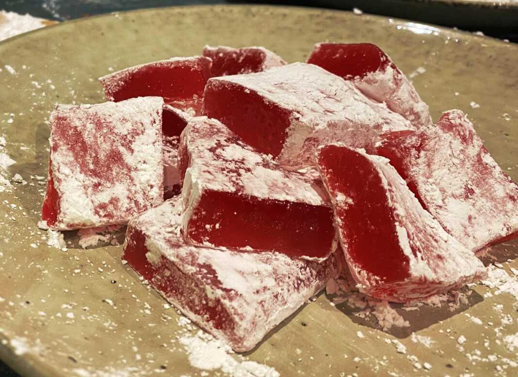 Μικρά τετράγωνα λουκούμια σε απαλό ροζ χρώμα, πλούσια πασπαλισμένα με άχνη ζάχαρη και κορν φλάουρ, τοποθετημένα σε μια πιατέλα.