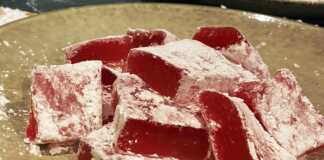 Σπιτικά Λουκούμια με Ροδόνερο Μικρά τετράγωνα λουκούμια σε απαλό ροζ χρώμα, πλούσια πασπαλισμένα με άχνη ζάχαρη και κορν φλάουρ, τοποθετημένα σε μια πιατέλα.