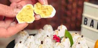 Μικρά αμυγδαλωτά σε σχήμα μανταρινιού, πασπαλισμένα με άχνη ζάχαρη και στολισμένα με ένα γαρύφαλλο στην κορυφή, τοποθετημένα σε πιατέλα.