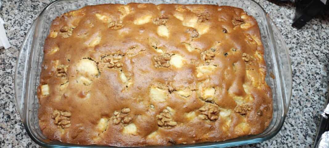 Μια ζουμερή μηλόπιτα σε πυρέξ, στολισμένη με ολόκληρα καρύδια στην επιφάνεια και περιχυμένη με χρυσάφι σιρόπι.