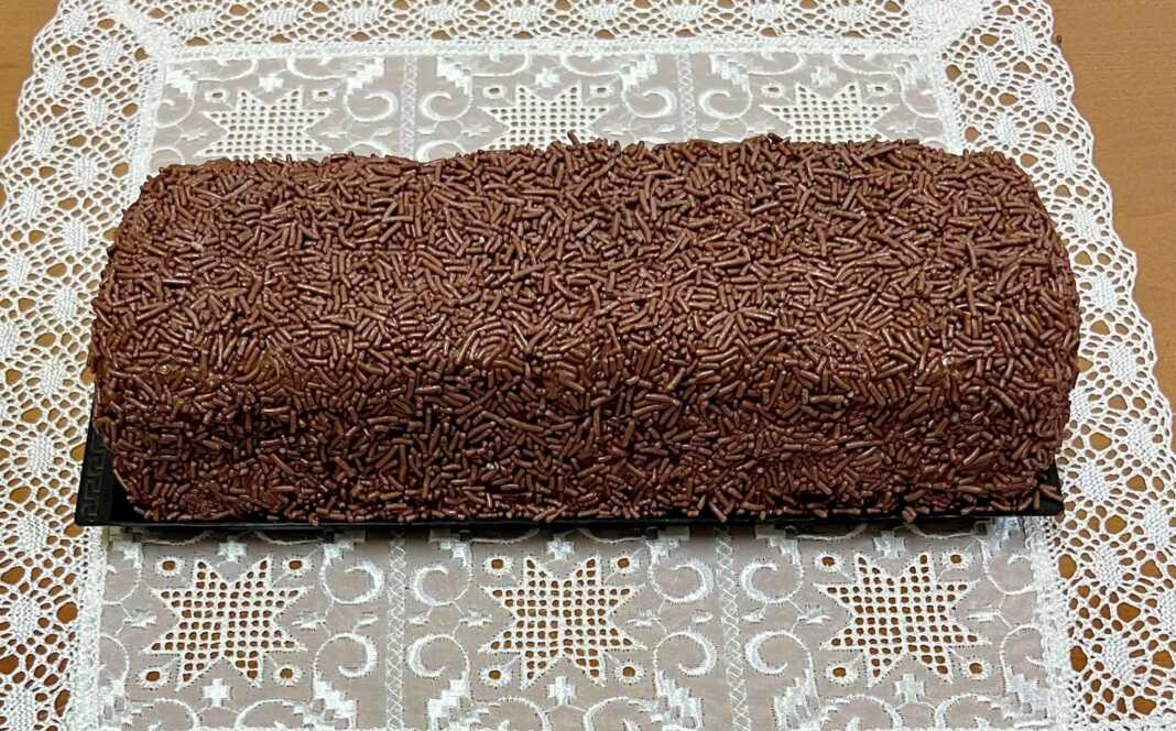 mosaiko Ένας λαχταριστός κορμός σοκολάτας πασπαλισμένος με τρούφα και νουτέλα, κομμένος σε φέτες που δείχνουν τα λευκά κομμάτια μπισκότου στο εσωτερικό του.