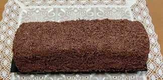 Κορμός Σοκολάτας – Μωσαϊκό: Η Απόλυτη Συνταγή με Ζαχαρούχο και Νουτέλα! Ένας λαχταριστός κορμός σοκολάτας πασπαλισμένος με τρούφα και νουτέλα, κομμένος σε φέτες που δείχνουν τα λευκά κομμάτια μπισκότου στο εσωτερικό του.