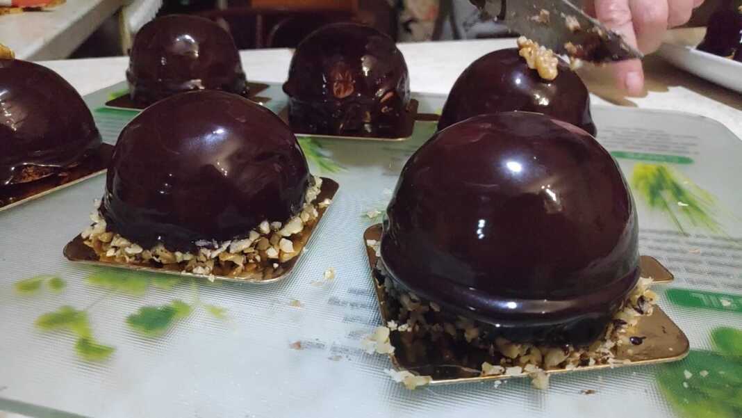 Κομψά ατομικά γλυκά μους καραμέλας καλυμμένα με γυαλιστερή επικάλυψη σοκολάτας, τοποθετημένα σε μια πιατέλα σερβιρίσματος.