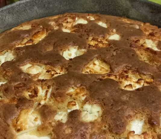 Μια χρυσαφένια καλαμποκόπιτα μέσα σε στρογγυλό ταψί, με λιωμένα κομμάτια φέτας στην επιφάνεια και τραγανή κρούστα.