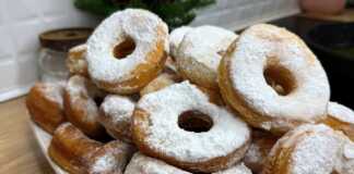 Μια στοίβα από φουσκωτά, χρυσαφένια ντόνατς, πλούσια πασπαλισμένα με λευκή ζάχαρη άχνη μέσα σε ένα βαθύ μπολ.