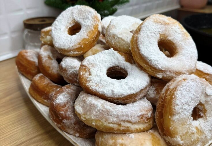 Μια στοίβα από φουσκωτά, χρυσαφένια ντόνατς, πλούσια πασπαλισμένα με λευκή ζάχαρη άχνη μέσα σε ένα βαθύ μπολ.