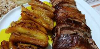 Ένα καλοψημένο ρολό χοιρινής πανσέτας κομμένο σε φέτες, με λιωμένη φέτα και πιπεριές στο κέντρο, δίπλα σε χρυσαφένιες πατάτες κυδωνάτες.