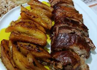 Ένα καλοψημένο ρολό χοιρινής πανσέτας κομμένο σε φέτες, με λιωμένη φέτα και πιπεριές στο κέντρο, δίπλα σε χρυσαφένιες πατάτες κυδωνάτες.