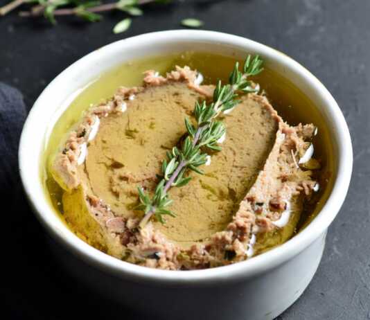 Ένα μικρό κεραμικό δοχείο με πατέ συκωτιού, καλυμμένο με μια στρώση χρυσαφένιου λιωμένου βουτύρου και ένα κλαδάκι θυμάρι από πάνω.