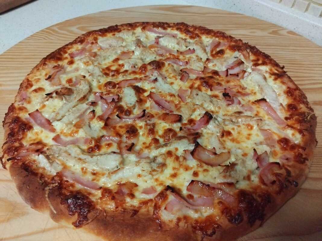 Μια λαχταριστή πίτσα με λευκή σάλτσα, κομμάτια κοτόπουλου, ξεροψημένο μπέικον και λιωμένη μοτσαρέλα.