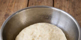 Μια φουσκωτή, λεία ζύμη πίτσας σε ένα μπολ, έτοιμη να ανοιχτεί και να γεμίσει με υλικά.