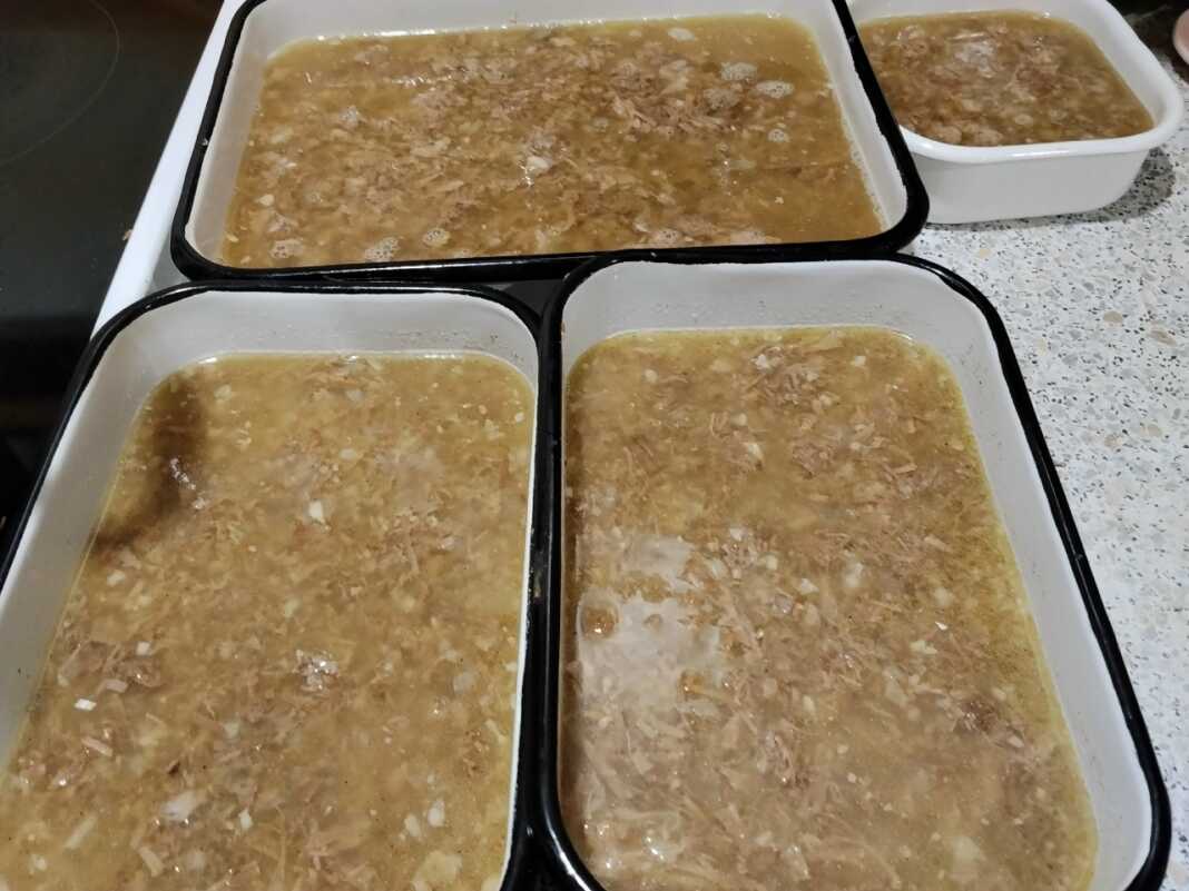 Διαυγές ζελέ πηχτής μέσα σε σκεύος, όπου διακρίνονται κομμάτια από τρυφερό χοιρινό κρέας και ψιλοκομμένο σκόρδο.