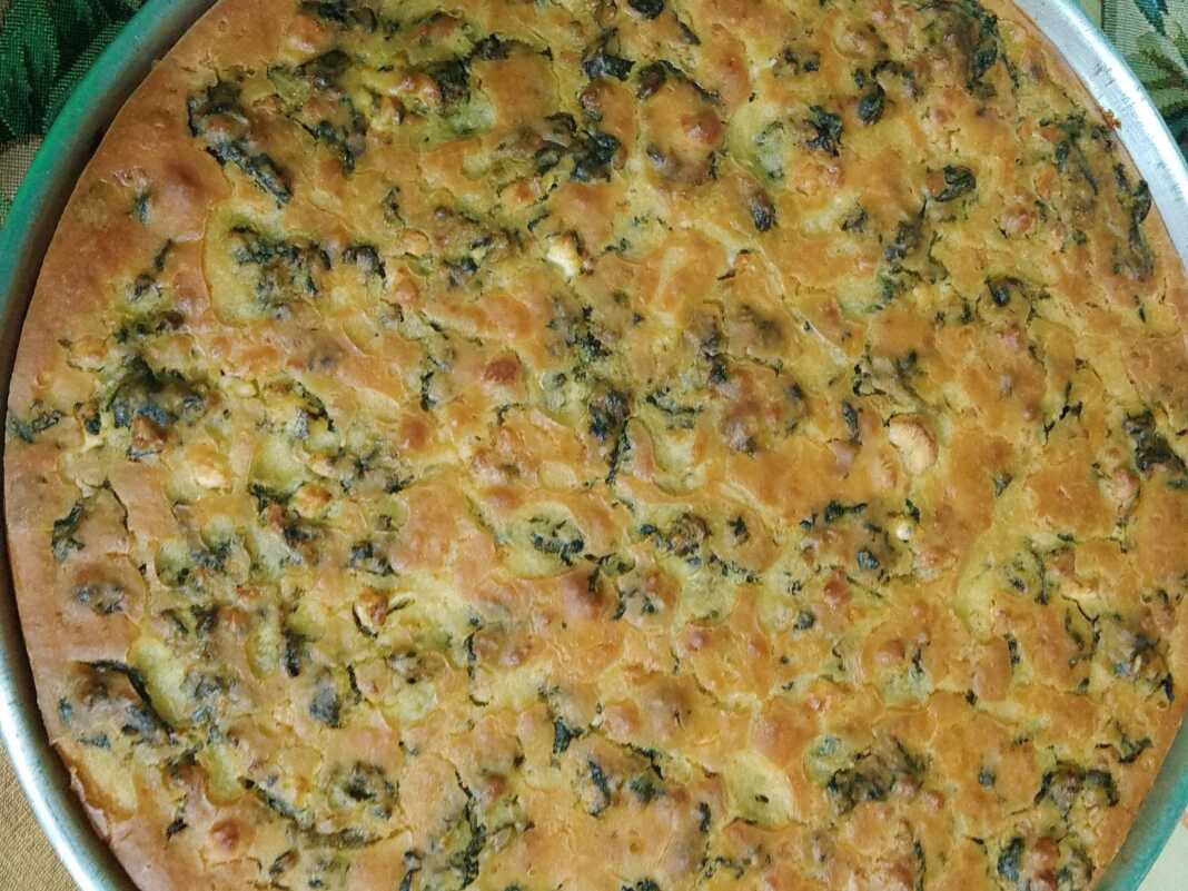 Ένα ταψί με παραδοσιακό πλαστό, με χρυσαφένια κρούστα από καλαμποκάλευρο και πλούσια πράσινη γέμιση από σπανάκι και μυρωδικά.