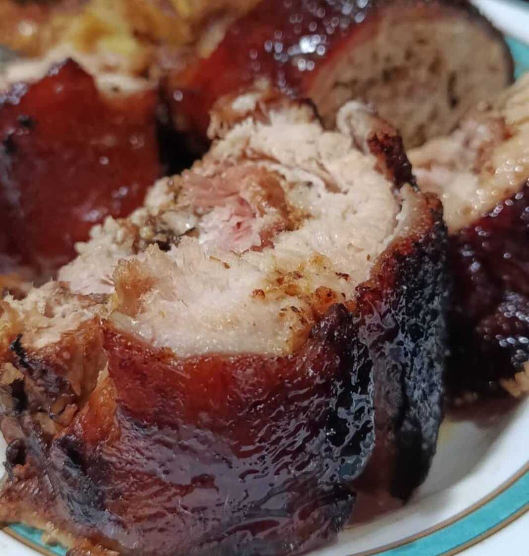 Ένα καλοψημένο ρολό χοιρινής πανσέτας με χρυσαφένια τραγανή πέτσα, δεμένο με σπάγκο και σερβιρισμένο με πατάτες φούρνου.