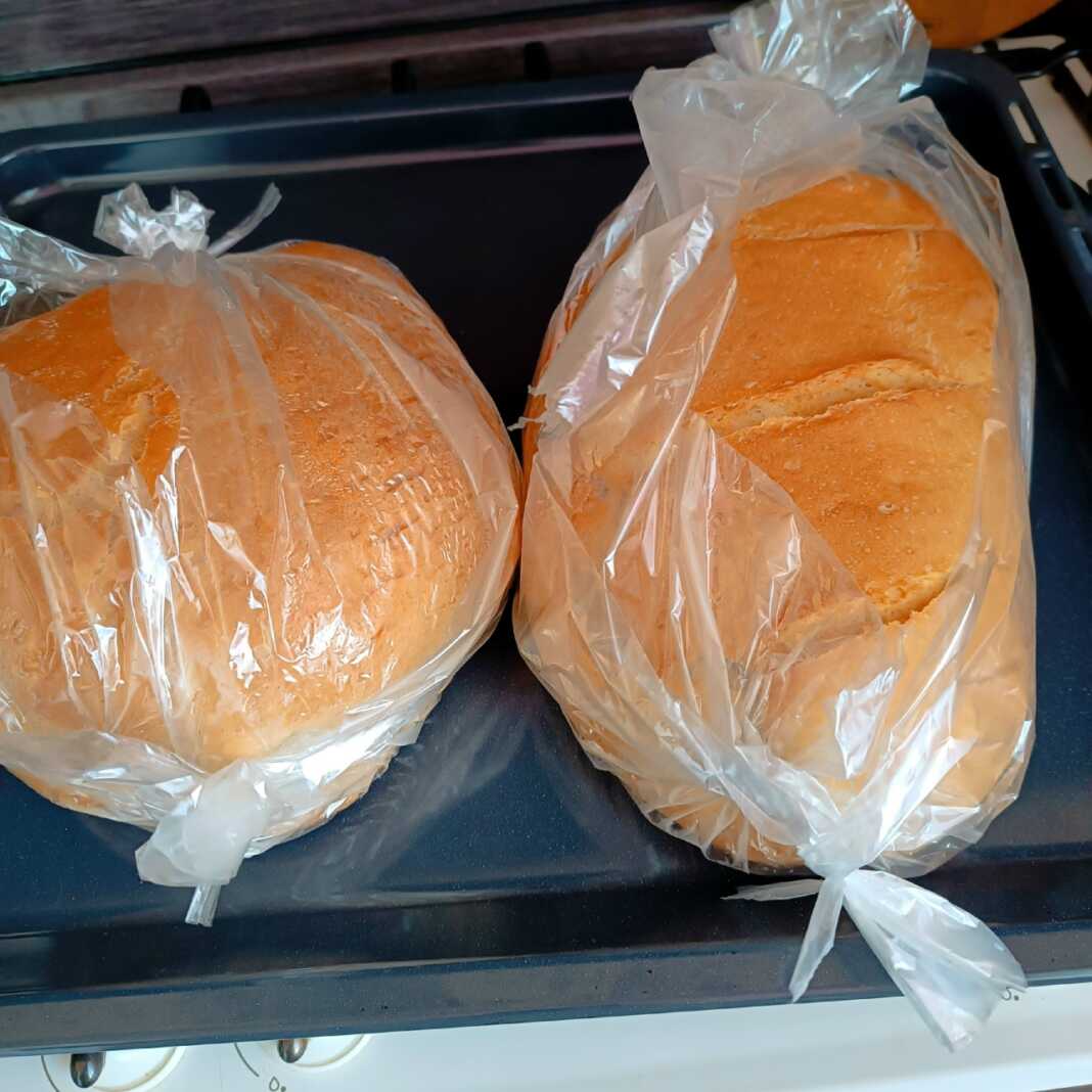 2 καρβέλια σπιτικό ψωμί με χρυσαφένια τραγανή κρούστα και βαθιά σκισίματα στην κορυφή, τοποθετημένο σε σακούλα