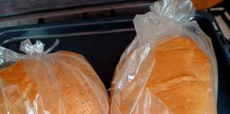 2 καρβέλια σπιτικό ψωμί με χρυσαφένια τραγανή κρούστα και βαθιά σκισίματα στην κορυφή, τοποθετημένο σε σακούλα