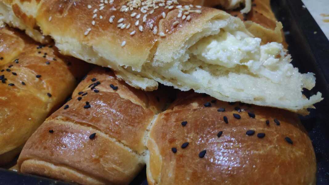 Σειρές από χρυσαφένια, αφράτα ρολάκια με τυρί, πασπαλισμένα με σουσάμι, μόλις βγήκαν από τον φούρνο.