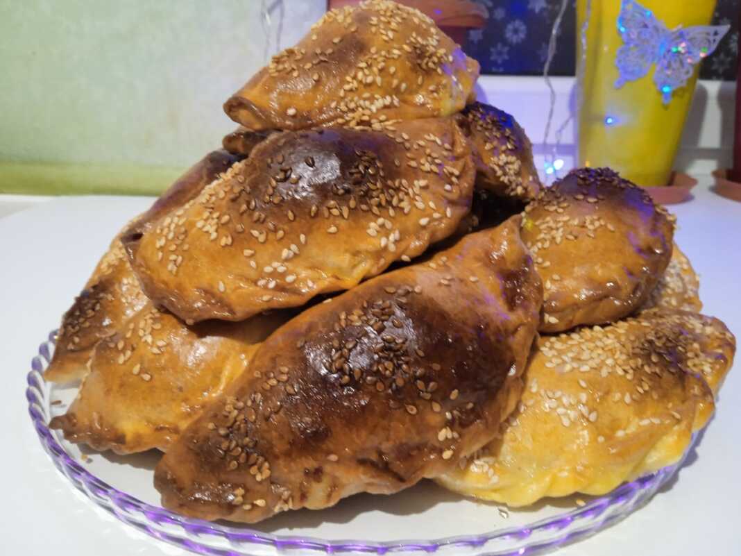 Σειρές από χρυσαφένια, τριγωνικά πιτάκια σαμσά πασπαλισμένα με μαύρο και λευκό σουσάμι πάνω σε λαδόκολλα.