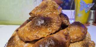 Σειρές από χρυσαφένια, τριγωνικά πιτάκια σαμσά πασπαλισμένα με μαύρο και λευκό σουσάμι πάνω σε λαδόκολλα.