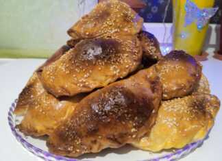 Σειρές από χρυσαφένια, τριγωνικά πιτάκια σαμσά πασπαλισμένα με μαύρο και λευκό σουσάμι πάνω σε λαδόκολλα.