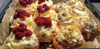 Δίσκος με αφράτα ρολά σιναμπόν καλυμμένα με λευκή κρέμα τυριού, μερικά με κανέλα και άλλα με κόκκινη γέμιση κερασιού.