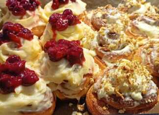 Δίσκος με αφράτα ρολά σιναμπόν καλυμμένα με λευκή κρέμα τυριού, μερικά με κανέλα και άλλα με κόκκινη γέμιση κερασιού.