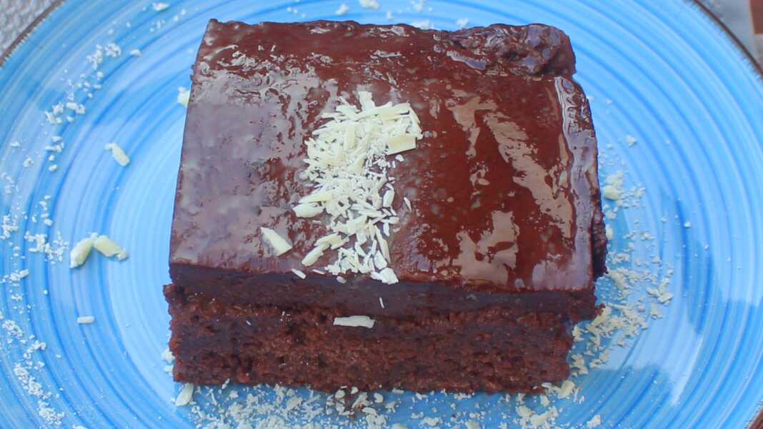 Ένα κομμάτι από εξαιρετικά υγρό κέικ σοκολάτας με πλούσιο σκούρο γλάσο, πασπαλισμένο με φιστίκι Αιγίνης.