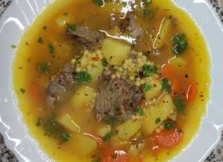 Ένα βαθύ πιάτο με αχνιστή μοσχαρόσουπα, κομμάτια τρυφερού κρέατος, πατάτες, καρότα και κουσκουσάκι, σερβιρισμένη με φρέσκο λεμόνι