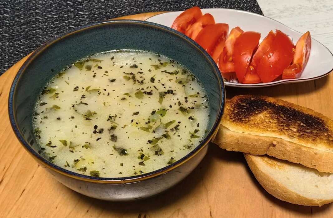 Ένα βαθύ πιάτο με κρεμώδη λευκή σούπα πατάτας, γαρνιρισμένο με φρέσκο μαϊντανό, τριμμένο τυρί και φρυγανισμένες φέτες ψωμιού.