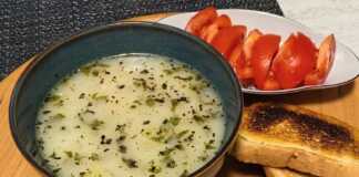 Ένα βαθύ πιάτο με κρεμώδη λευκή σούπα πατάτας, γαρνιρισμένο με φρέσκο μαϊντανό, τριμμένο τυρί και φρυγανισμένες φέτες ψωμιού.