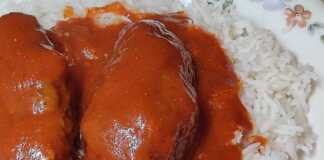 Ένα πιάτο με μελωμένα σουτζουκάκια σε πλούσια κόκκινη σάλτσα, σερβιρισμένα πάνω σε αφράτο ρύζι μπασμάτι.