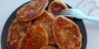 Μια στοίβα από χρυσαφένιες τηγανίτες, περιχυμένες με μέλι και πασπαλισμένες με κανέλα και καρύδια.