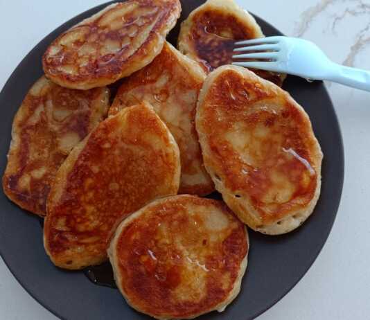 Μια στοίβα από χρυσαφένιες τηγανίτες, περιχυμένες με μέλι και πασπαλισμένες με κανέλα και καρύδια.