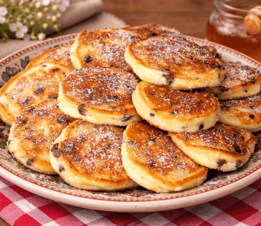 Μια στοίβα από αφράτες, χρυσαφένια τηγανίτες με λιωμένες σταγόνες σοκολάτας στο εσωτερικό τους, σερβιρισμένες σε ένα λευκό πιάτο.