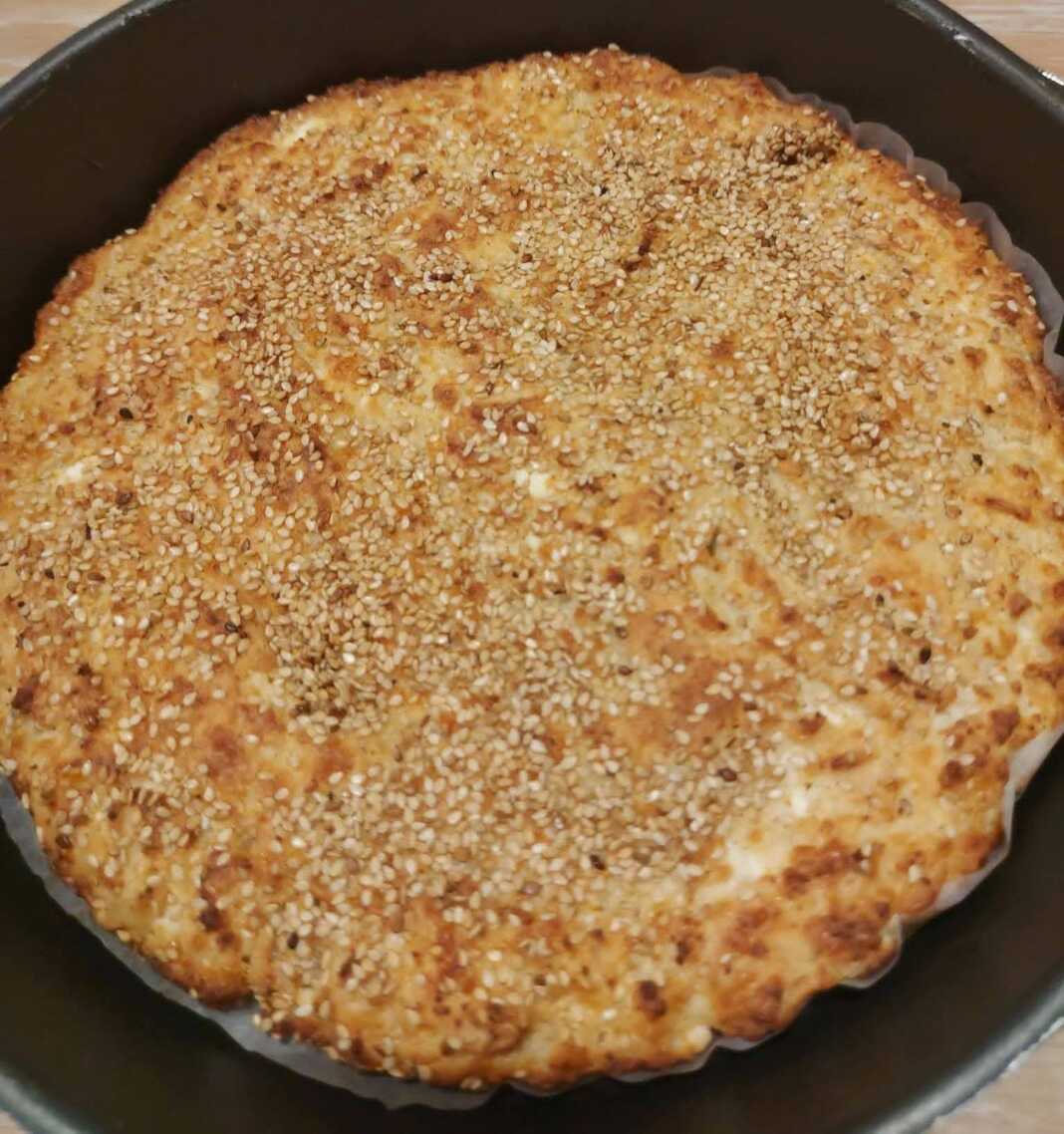 Μια ροδοκοκκινισμένη τυρόπιτα πασπαλισμένη με σουσάμι, κομμένη σε κομμάτια μέσα στο ταψί της.