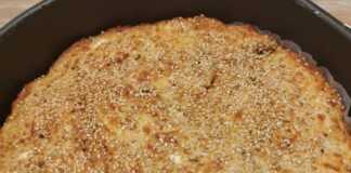 Μια ροδοκοκκινισμένη τυρόπιτα πασπαλισμένη με σουσάμι, κομμένη σε κομμάτια μέσα στο ταψί της.