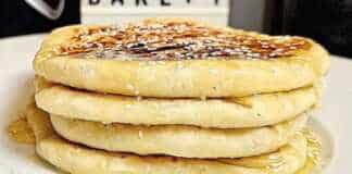 Ζεστά και χρυσαφένια τυρόψωμα στο πιάτο, περιχυμένα με ρευστό μέλι και πασπαλισμένα με καβουρδισμένο σουσάμι.