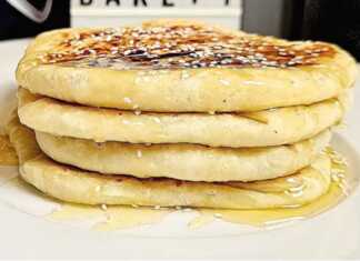 Ζεστά και χρυσαφένια τυρόψωμα στο πιάτο, περιχυμένα με ρευστό μέλι και πασπαλισμένα με καβουρδισμένο σουσάμι.