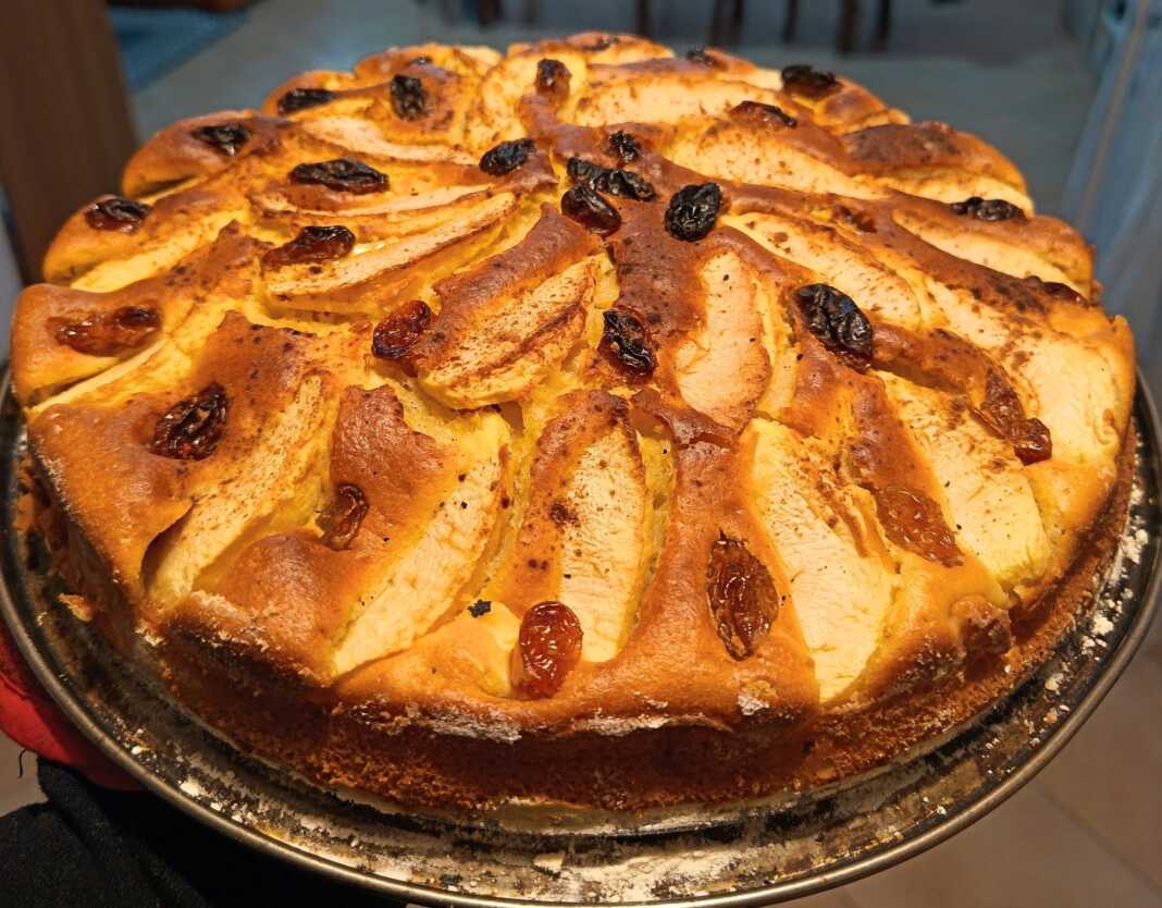 Μια χρυσαφένια μηλόπιτα διακοσμημένη με λεπτές φέτες μήλου και σταφίδες, πασπαλισμένη με κανέλα.