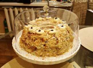 Μια εντυπωσιακή τούρτα σε σχήμα στεφανιού, καλυμμένη με λευκή κρέμα και πλούσιο καβουρδισμένο φιλέ αμυγδάλου, στολισμένη με κόκκινα κεράσια.