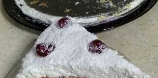 Μια εντυπωσιακή λευκή τούρτα καλυμμένη με πλούσιο ινδοκάρυδο, διακοσμημένη με κόκκινα κερασάκια σε χιονισμένο φόντο.