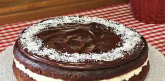 Ένα ψηλό σοκολατένιο κέικ με μια λευκή στρώση κρέμας καρύδας στη μέση, καλυμμένο με γυαλιστερή σοκολάτα και πασπαλισμένο με ινδοκάρυδο.