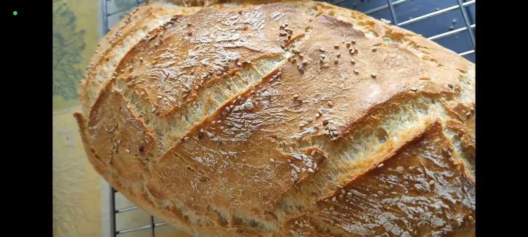 Ένα καρβέλι χωριάτικο ψωμί μέσα σε πυρακτωμένη μαντεμένια γάστρα, με έντονα σκασίματα στην επιφάνεια και χρυσαφένιο χρώμα.