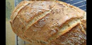 Ένα καρβέλι χωριάτικο ψωμί μέσα σε πυρακτωμένη μαντεμένια γάστρα, με έντονα σκασίματα στην επιφάνεια και χρυσαφένιο χρώμα.