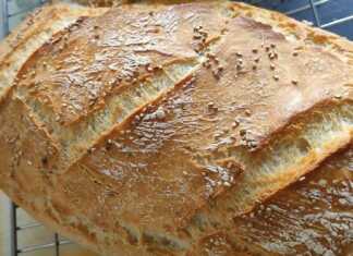 Ένα καρβέλι χωριάτικο ψωμί μέσα σε πυρακτωμένη μαντεμένια γάστρα, με έντονα σκασίματα στην επιφάνεια και χρυσαφένιο χρώμα.