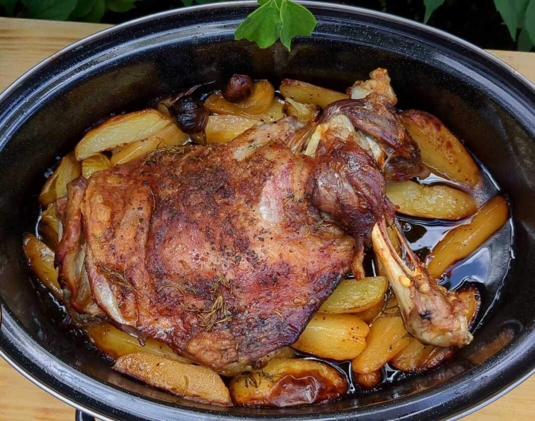 Μια ανοιχτή γάστρα με ροδοκοκκινισμένο αρνί και μελωμένες πατάτες, περιχυμένα με τη σάλτσα τους και φρέσκο δεντρολίβανο.