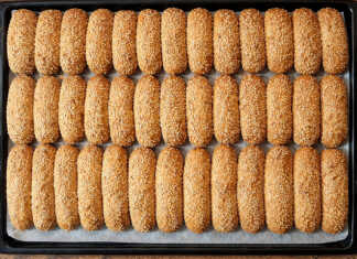 Χρυσαφένια κουλουράκια λεμονιού πασπαλισμένα με σουσάμι τοποθετημένα μέσα σε ταψί