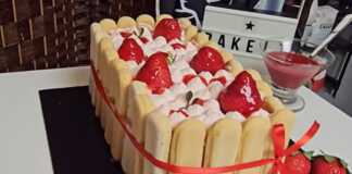 Ένα εντυπωσιακό τιραμισού με φράουλες, δεμένο με κορδέλα και περιχυμένο με κατακόκκινη σάλτσα φράουλας.