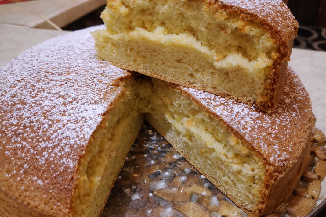 Ένα ψηλό και εξαιρετικά αφράτο κέικ πασπαλισμένο με άχνη ζάχαρη, κομμένο σε τριγωνικά κομμάτια.